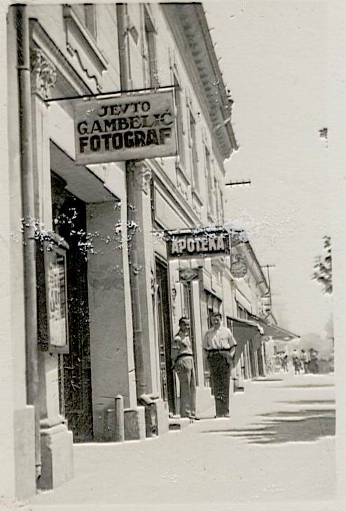 Na staroj fotografiji s druge polovine 20. veka vidi se centar Stare Pazove, dom porodice Lovodić, reklama pazovačkog fotografa Jefte Gambelića, apoteka i dva čoveka ispred zgrade.